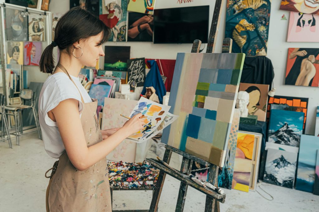 A woman creating abstract art in a vibrant studio with various paintings in the background.